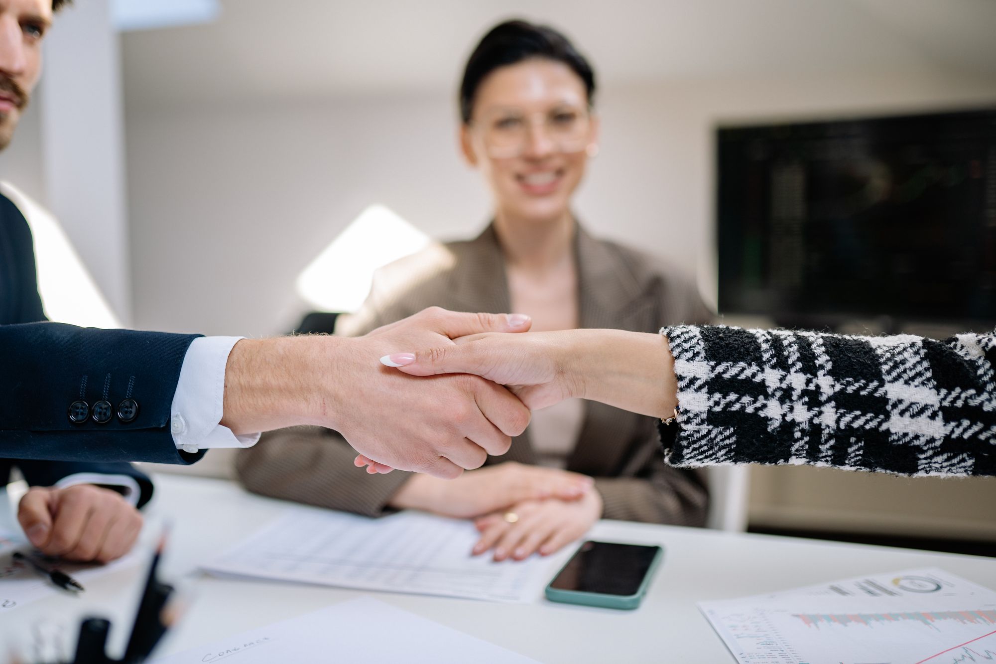Preisstrategie in der Verhandlung: Geschäftspartner besiegeln Einigung per Handschlag am Besprechungstisch