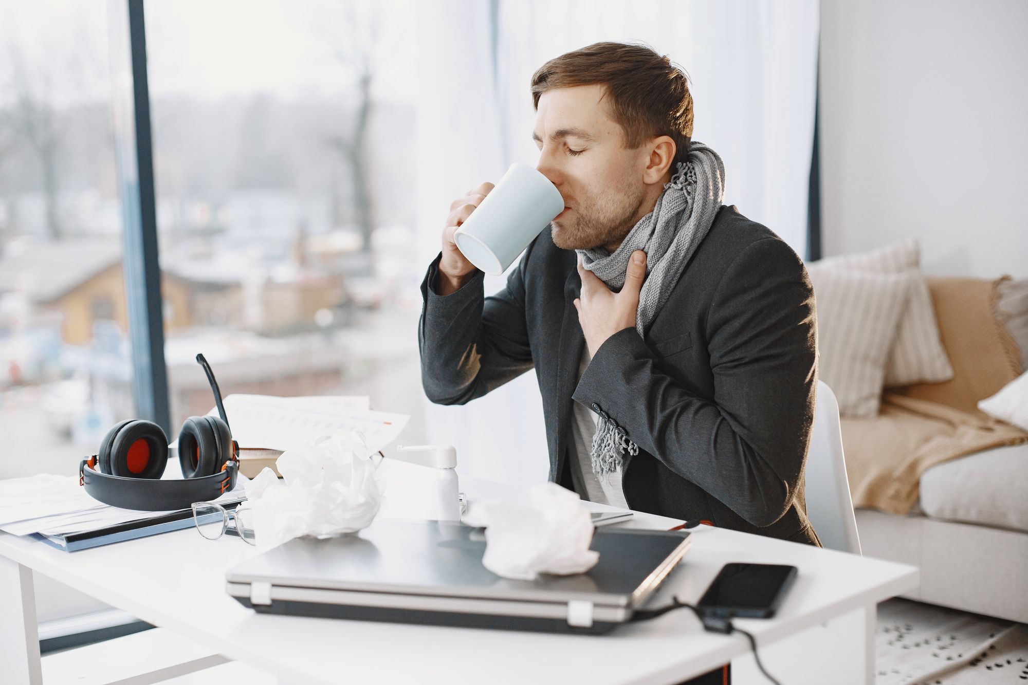 Kranker Mann sitzt am Schreibtisch und trinkt aus einer Tasse, Symbolbild für hohen Krankenstand