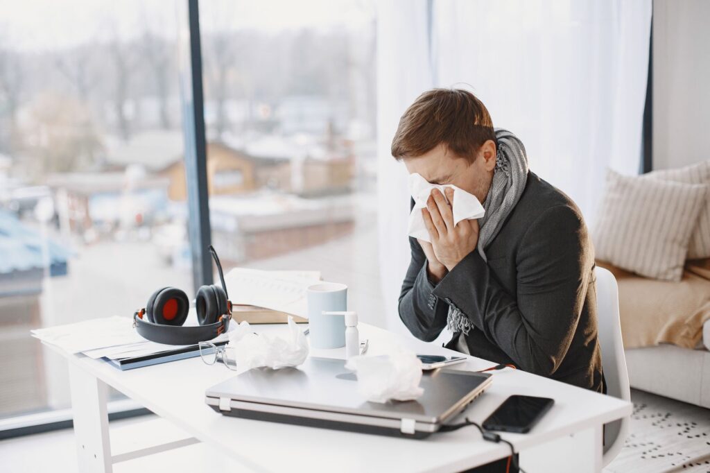Krankschreibung im Büro: Kranker Mann sitzt am Schreibtisch und niest