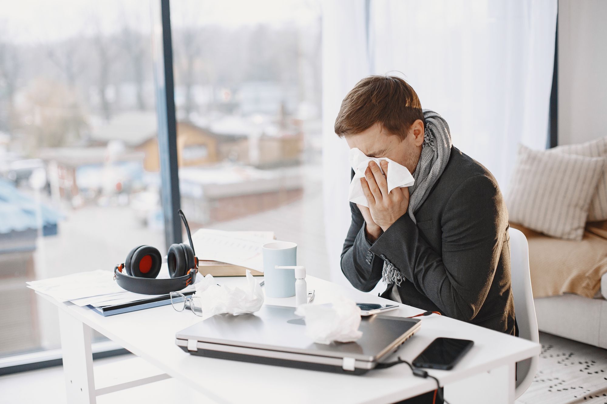 Krankschreibung im Büro: Kranker Mann sitzt am Schreibtisch und niest
