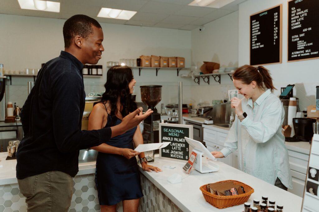 Kunden sprechen mit einer Kassiererin im Café, typischer Arbeitsplatz im Minijob 2027