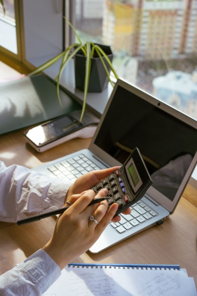 Unternehmenswert berechnen: Person nutzt Taschenrechner und Laptop am Schreibtisch